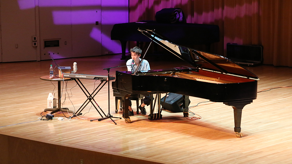 Jacob Collier addresses the crowd at the Frost School of Music while setting at a piano