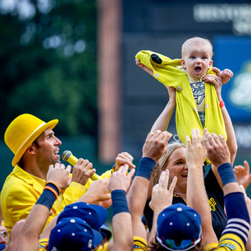 Molly Knutson holds her baby James Knutson high above the players as the Savannah Bananas present the Banana Baby to the crowd while playing the theme song from the movie "Lion King" over the public address system, Saturday, June 11, 2022, in Savannah, Ga. (AP Photo/Stephen B. Morton)