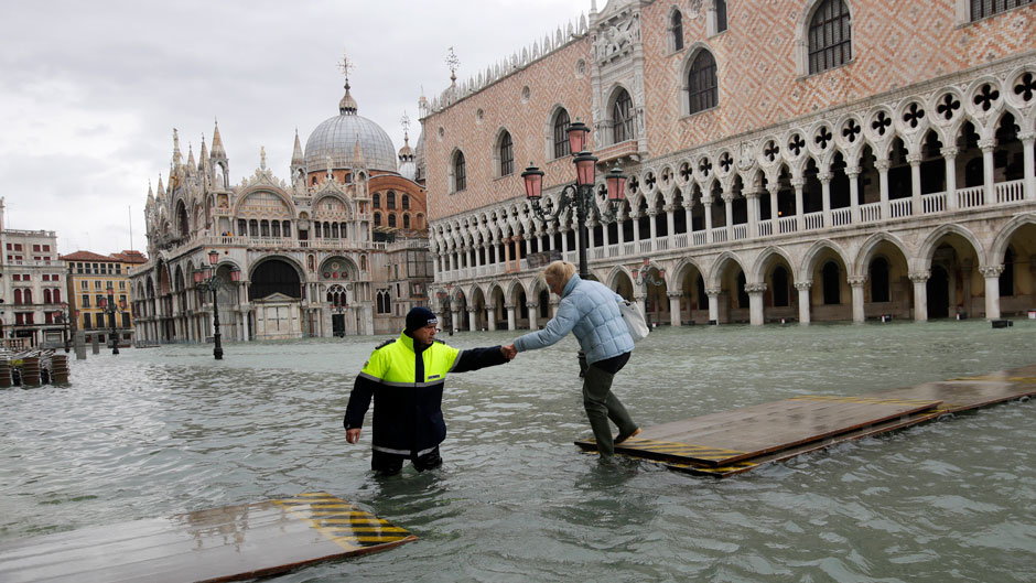 A city worker helps a woman who decided to cross St. Mark square on a gangway, in spite of prohibition, in Venice, Italy, Sunday, Nov. 17, 2019. Venetians are bracing for the prospect of another exceptional tide in a season that is setting new records. Officials are forecasting a 1.6 meter (5 feet, 2 inches) surge Sunday. That comes after Tuesday's 1.87 meter flood, the worst in 53 years, followed by high tide of 1.54 meters on Friday. (AP Photo/Luca Bruno)