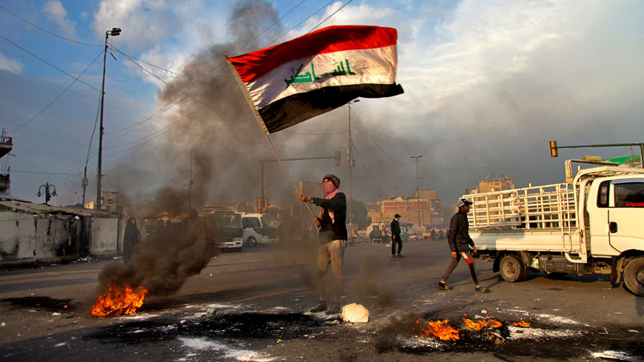 A protester waves the Iraq flag while demonstrators set fire to close streets near Tahrir Square during a demonstration to protest against the Iranian missile strike, in Baghdad, Iraq, Wednesday, Jan. 8, 2020. Iran struck back at the United States early Wednesday for killing a top Revolutionary Guard commander, firing a series of ballistic missiles at two military bases in Iraq that house American troops in a major escalation between the two longtime foes. (AP Photo/Khalid Mohammed)