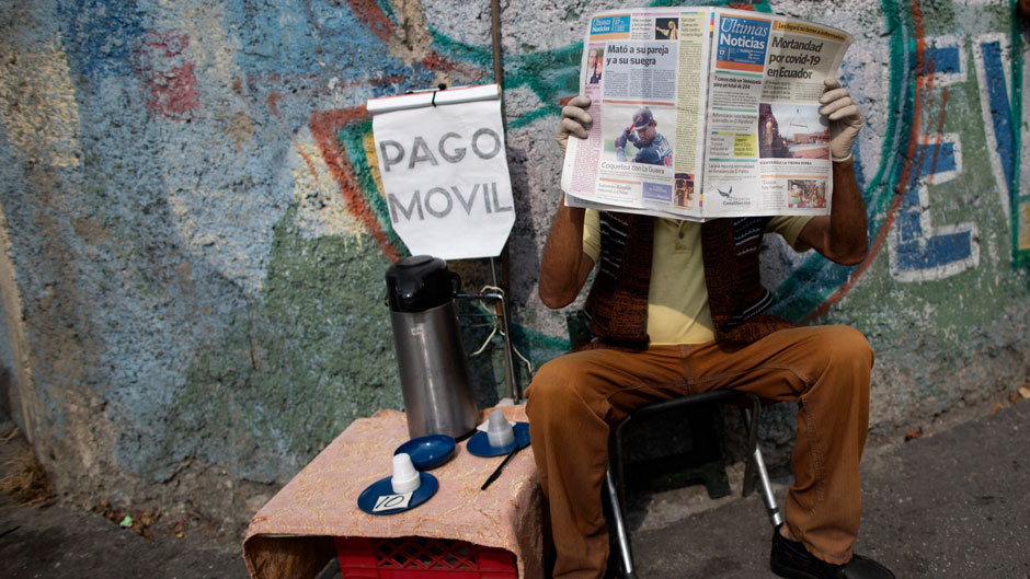 An informal coffee vendor reads a newspaper with a headline that reads in Spanish: "COVID-19 mortality in Ecuador" as he waits for clients during a nationwide quarantine to help curb the spread of the new coronavirus, in Caracas, Venezuela, Friday, April 17, 2020. (AP Photo/Ariana Cubillos)