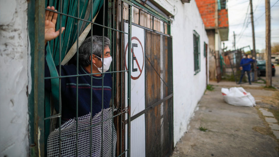 A man peers from his home as police set up fences, behind right, to isolate the Villa Azul neighborhood after over 50 residents tested positive for the new coronavirus, according to government health officials, on the outskirts of Buenos Aires, Argentina, Monday, May 25, 2020. (AP Photo/Natacha Pisarenko)