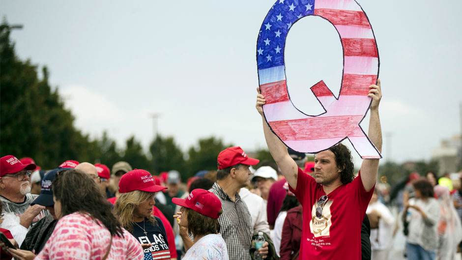 In this Aug. 2, 2018, file photo, a protesters holds a Q sign waits in line with others to enter a campaign rally with President Donald Trump in Wilkes-Barre, Pa. Facebook and Twitter promised to stop encouraging the growth of the baseless conspiracy theory QAnon, which fashions President Donald Trump as a secret warrior against a supposed child-trafficking ring run by celebrities and government officials. But the social media companies haven’t succeeded at even that limited goal, a review by The Associated Press found. (AP Photo/Matt Rourke, File)