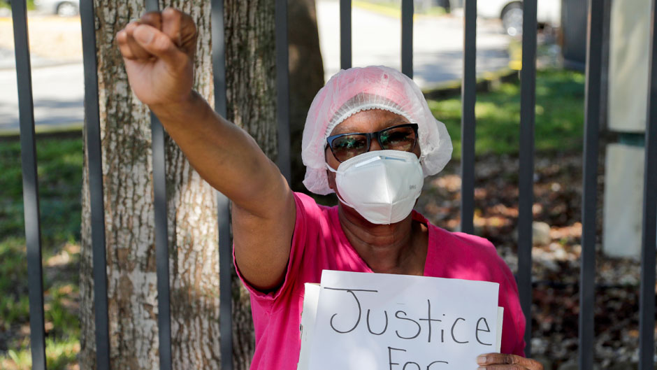 Lillie Roberson raises her arm as she kneels outside of the Sinai Plaza Rehabilitation and Nursing Center, where she works as a secretary, during a protest in the memory of George Floyd, Thursday, June 11, 2020, in Miami. Protests continue over the death of Floyd, a black man who died while in police custody in Minneapolis. (AP Photo/Lynne Sladky)