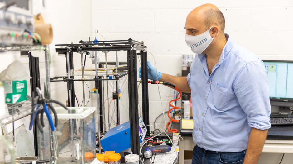 Emrah Celik, who developed a new additive manufacturing technique to produce a durable thermoset composite, checks on a 3D printer as it extrudes fiber-reinforced composite ink. 