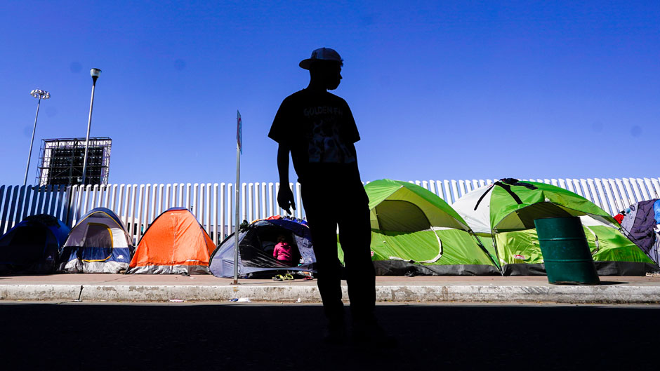 A migrant from Honduras seeking asylum in the United States stands in front of rows of tents at the border crossing, Monday, March 1, 2021, in Tijuana, Mexico. President Joe Biden is holding a virtual meeting with Mexican President Andrés Manuel López Obrador. Monday's meeting was a chance for them to discuss migration, among other issues. (AP Photo/Gregory Bull)