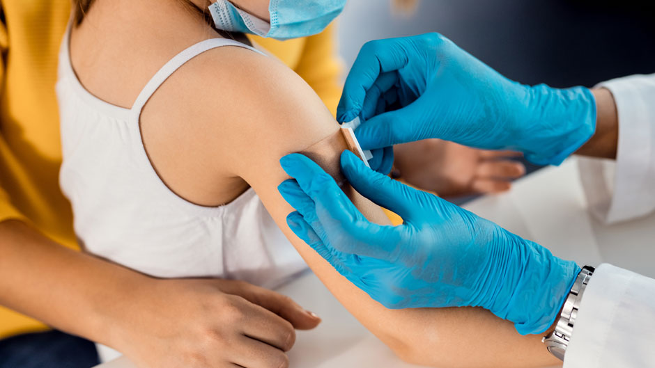 Stock image of a doctor placing a bandage on a child's arm following a routine vaccine appointment.