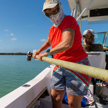 Kathleen Sullivan Sealey guides a long fiberglass tube holding clear plastic sample bottles over the edge of an open fisherman boat in the Florida Keys. Photos: Janette Neuwahl Tannen/University of Miami
