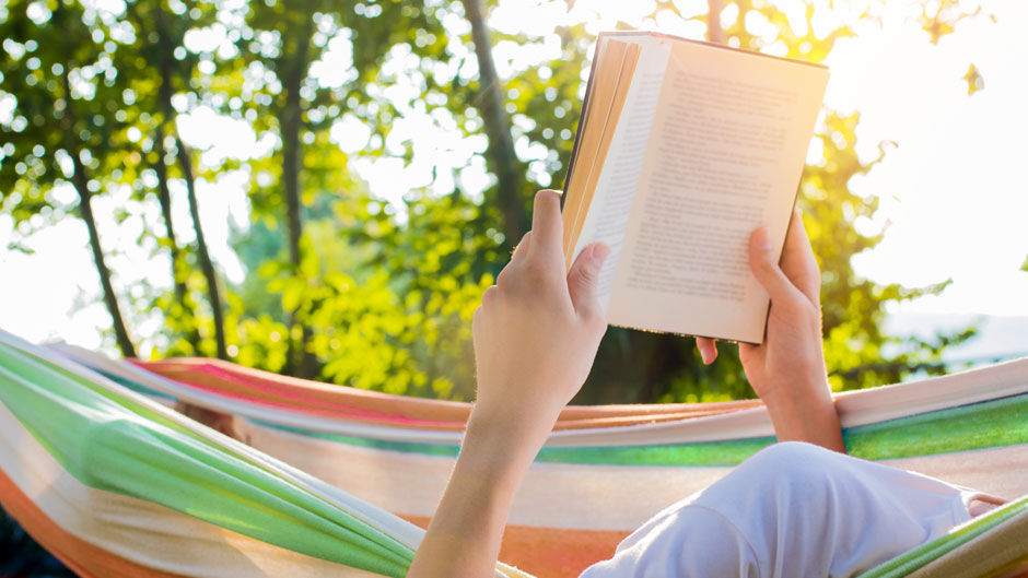 Stock photo. A person reading in a hammock with an open book.