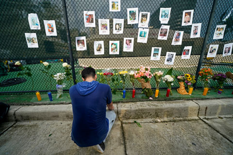Leo Soto, who created this memorial with grocery stores donating flowers and candles, pauses in front of photos of some of the missing people that he put on a fence, near the site of an oceanfront condo building that partially collapsed in Surfside, Fla., Friday, June 25, 2021. (AP Photo/Gerald Herbert)