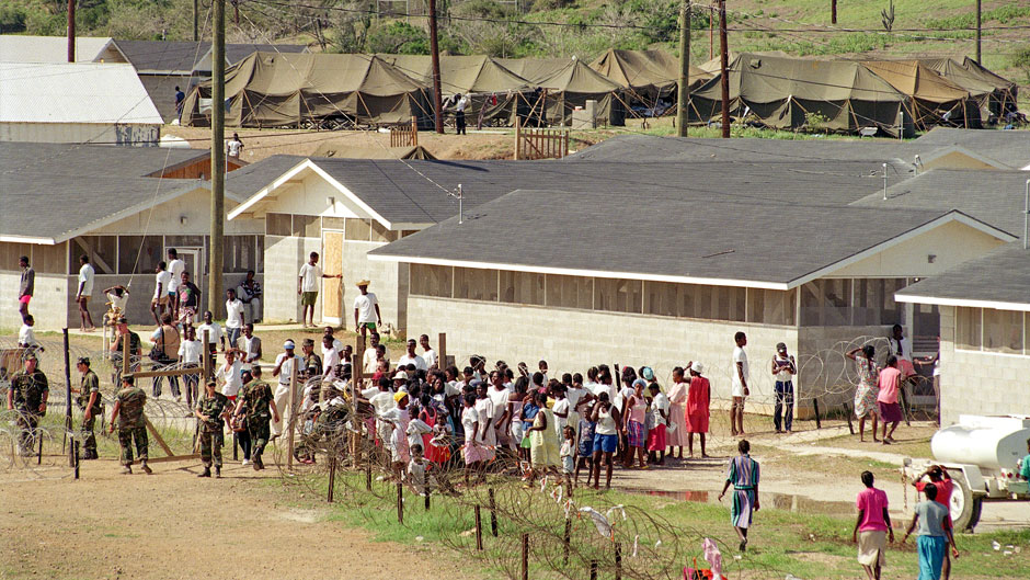 Haitian refugees gather at the entrance to Camp Bulkeley, a tent city at Guantanamo Bay Naval Base in Cuba on Nov. 27, 1991. Rescues continue at sea for Haitians fleeing the worsening economic hardships. Tents set up to house the refugees can be seen in the background. U.S. officials fear overcrowding by the end of the week. (AP Photo/Greg Gibson)
