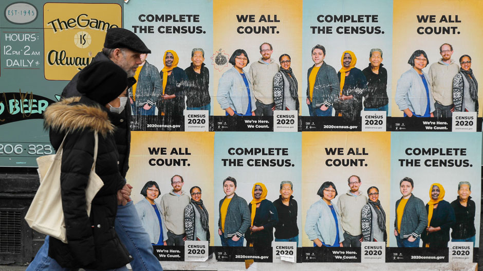In this Wednesday, April 1, 2020 file photo, people walk past posters encouraging participation in the 2020 Census in Seattle's Capitol Hill neighborhood. From McKenzie County, North Dakota to St. Johns County Florida, the growth in the number of people who identified as multiracial on 2020 census responses soared over the last decade, rising from under 3% to more than 10% of the U.S. population from 2010 and 2020.(AP Photo/Ted S. Warren, File)