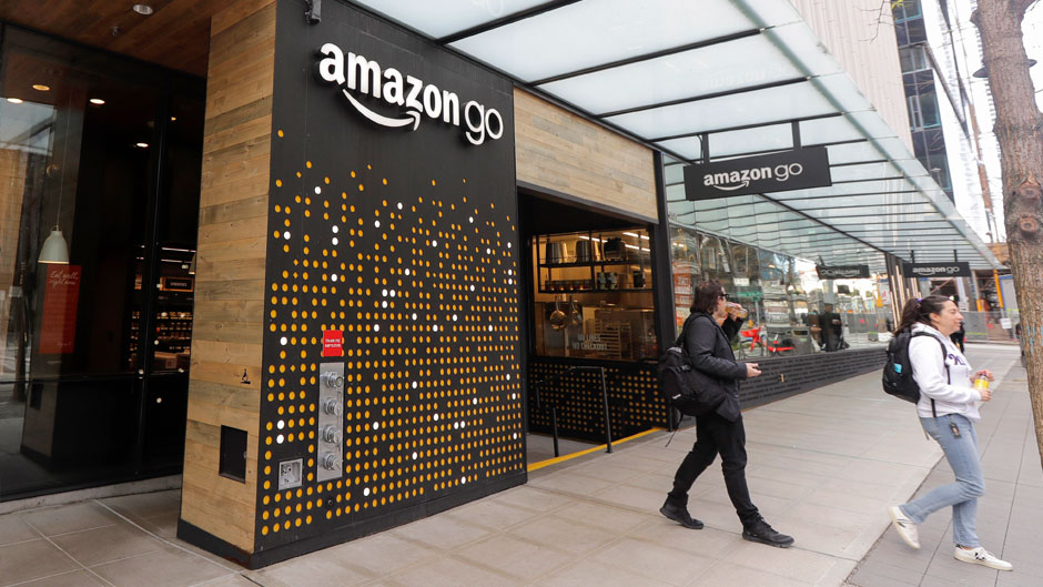 In this March 4, 2020 file photo, people walk out of an Amazon Go store, in Seattle. Amazon is rolling out a new device for contactless transactions that will scan an individual’s palm. The Amazon One, which will initially launch in two Amazon Go stores in Seattle, is being viewed as a way for people to use their palm to make everyday activities like paying at a store easier. (AP Photo/Ted S. Warren, File)