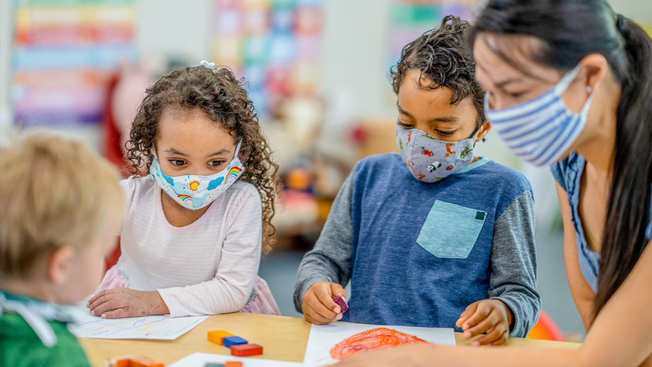 Multi-ethnic group of children coloring at a table while wearing protective face masks to avoid the transfer of germs.