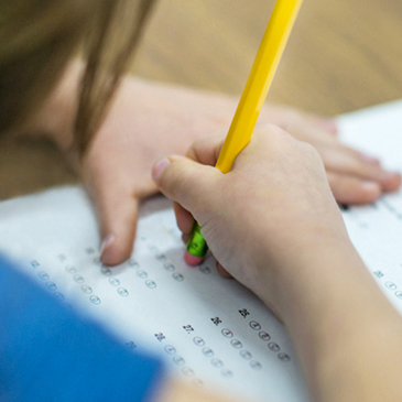Stock image of a young student taking an exam using a pencil.