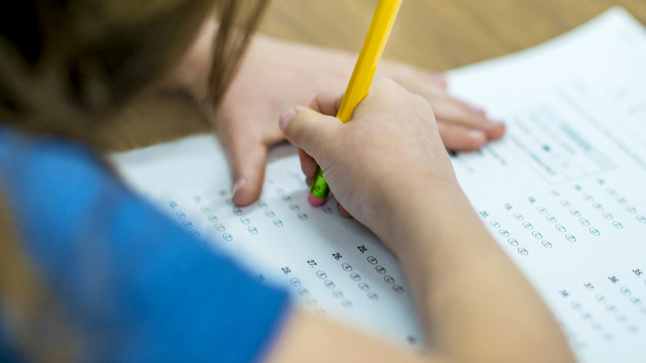 Stock image of a young student taking an exam using a pencil.