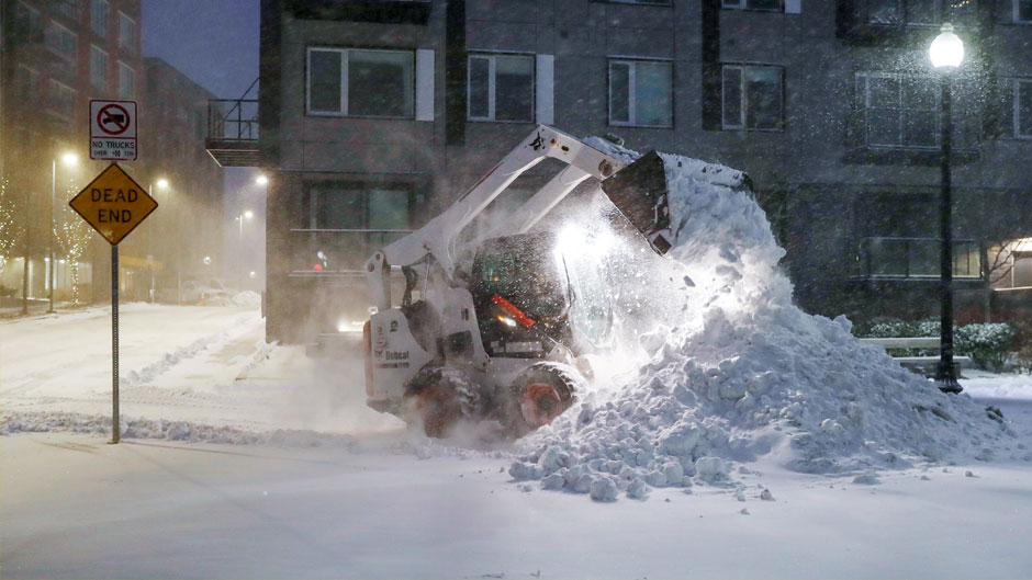 A frontend loader removes snow at Clipper Ship Wharf in the East Boston neighborhood of Boston. People from New York City to Maine are awakening to deep snow and high winds as a powerful nor’easter kicks up blizzard conditions. (AP Photo/Michael Dwyer)