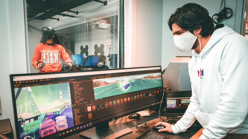 A programmer edits a VR app, while the creator, University of Miami senior Léa Dorne, tests it out in the background. Photo: Mike Montero/University of Miami