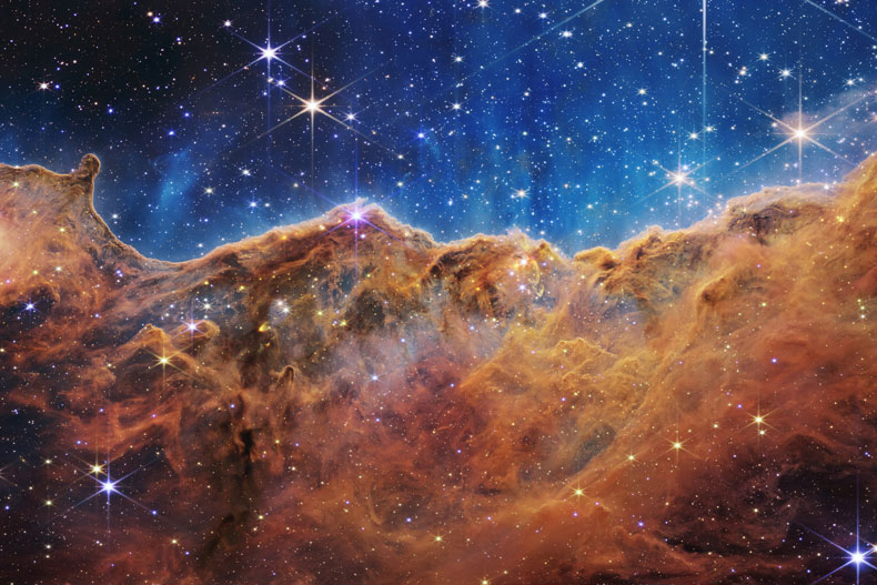 This landscape of “mountains” and “valleys” speckled with glittering stars is actually the edge of a nearby, young, star-forming region called NGC 3324 in the Carina Nebula. Credits: NASA, ESA, CSA, and STScI