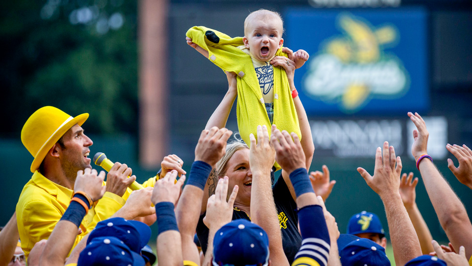 Molly Knutson holds her baby James Knutson high above the players as the Savannah Bananas present the Banana Baby to the crowd while playing the theme song from the movie "Lion King" over the public address system, Saturday, June 11, 2022, in Savannah, Ga. (AP Photo/Stephen B. Morton)