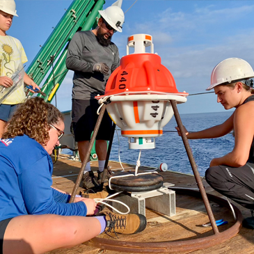 Graduate students Rachel Sampson and Paloma Cartwright and undergraduate oceanography student Allie Cook work with mooring technician Eduardo Jardim to prepare a CPIES monitoring device for deployment. Photo: Courtesy of Lisa Beal