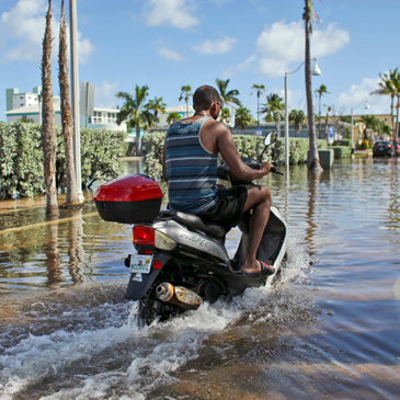 A motorbike navigates through floodwater caused by a seasonal king tide, Monday, Oct. 17, 2016, in Hollywood, Fla. King tides bring in unusually high water levels and can cause local tidal flooding. (AP Photo/Lynne Sladky)