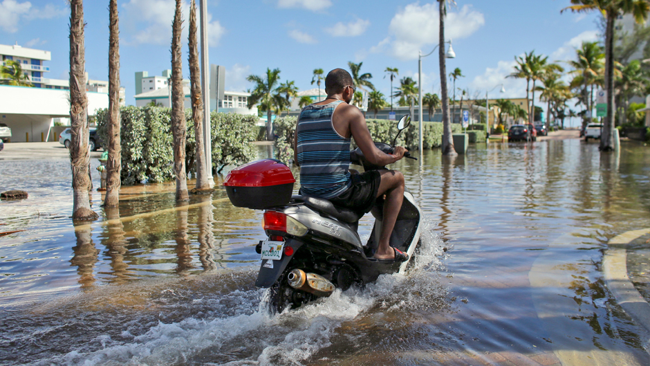 A motorbike navigates through floodwater caused by a seasonal king tide, Monday, Oct. 17, 2016, in Hollywood, Fla. King tides bring in unusually high water levels and can cause local tidal flooding. (AP Photo/Lynne Sladky)