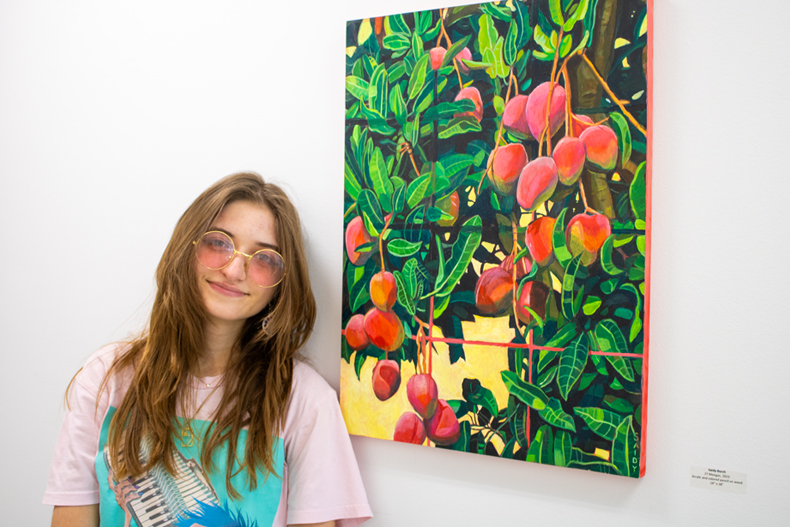 Saidy Burch poses with her piece, “27 Mangos,” acrylic and colored pencil on wood. Photo: Bianca Sproul for University of Miami