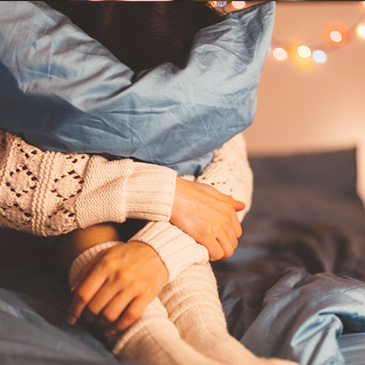 Stock image shows a woman in beg hugging a pillow to symbolize feeling anxious during the holidays 