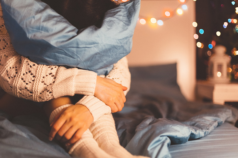 Stock image shows a woman in beg hugging a pillow to symbolize feeling anxious during the holidays 