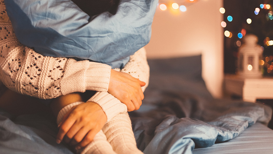 Stock image shows a woman in beg hugging a pillow to symbolize feeling anxious during the holidays