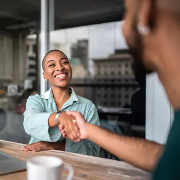 Two people shaking hands while sitting at a table 
