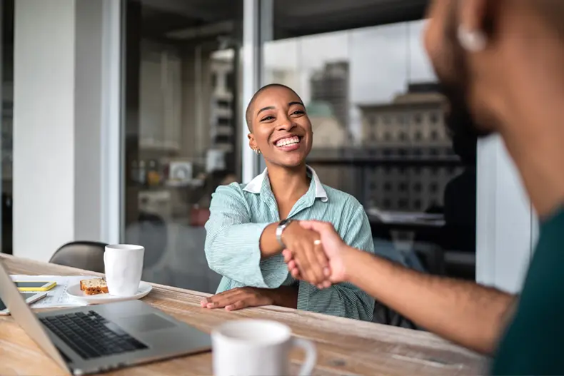 Two people shaking hands while sitting at a table 