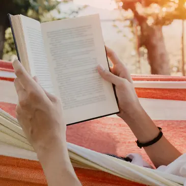Person laying in a hammock reading a book