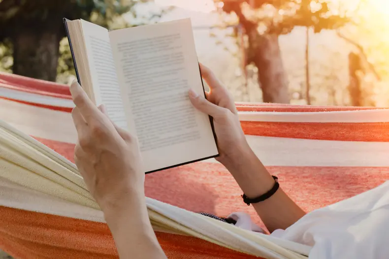 Person laying in a hammock reading a book