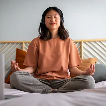 Student sitting on bed wearing headphones while meditating. 