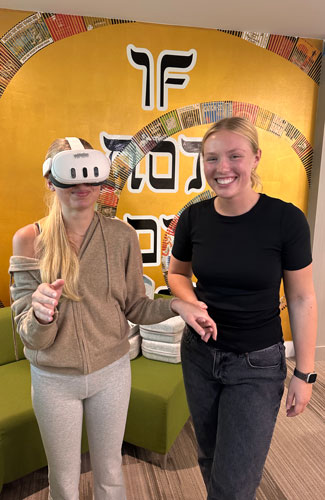 A student guides another student wearing a virtual reality headset