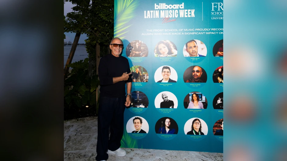 Legendary music producer Emilio Estefan, an honorary degree holder and member of the  the Dean’s Advisory Committee at the Frost School, poses with his photo on the display of Frost School alumni for Billboard Latin Music Week.